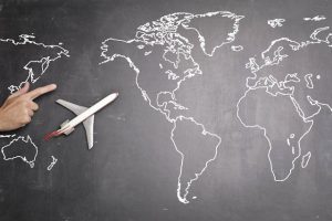 A hand pointing at a chalk-drawn map of the world with a model airplane on it, symbolizing travel.