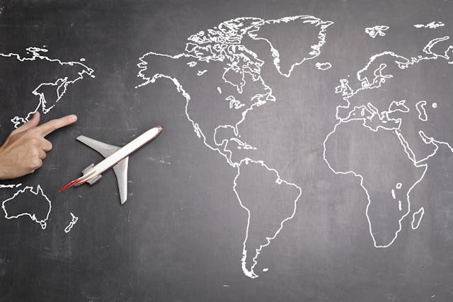 A hand pointing at a chalk-drawn map of the world with a model airplane on it, symbolizing travel.